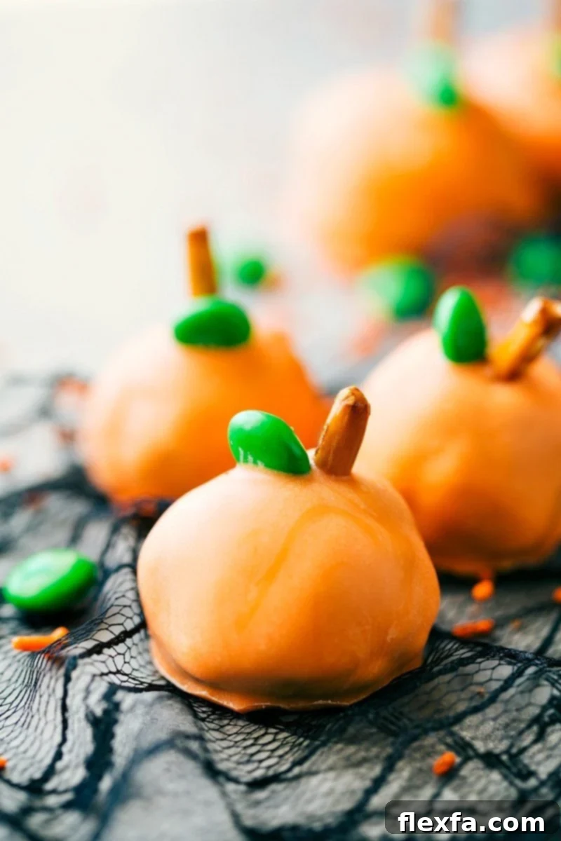 Bright orange Pumpkin Oreo Truffles, decorated with green M&M's and pretzel stems, on a Halloween-themed background.