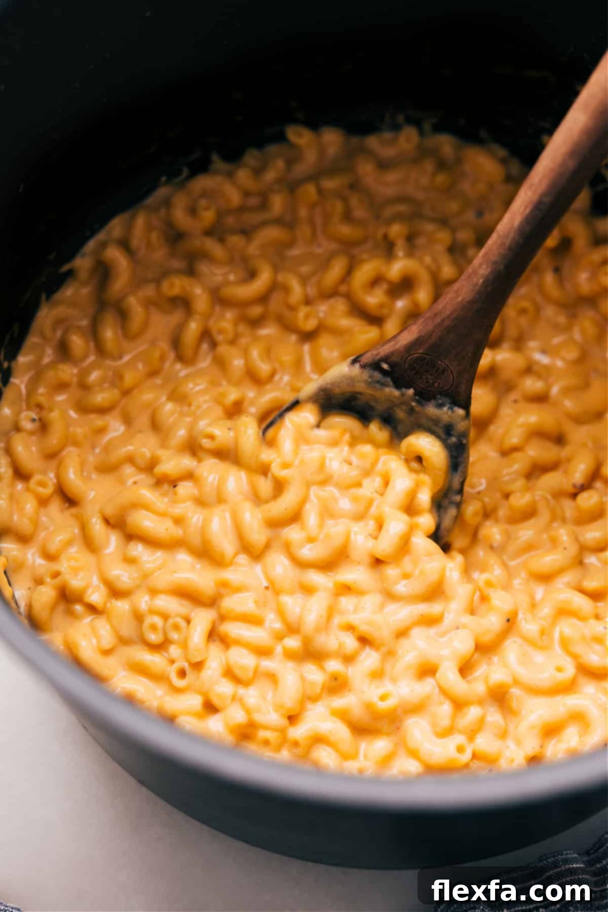 A large pot brimming with rich, creamy one-pot mac and cheese, with a serving spoon poised to scoop out a portion.