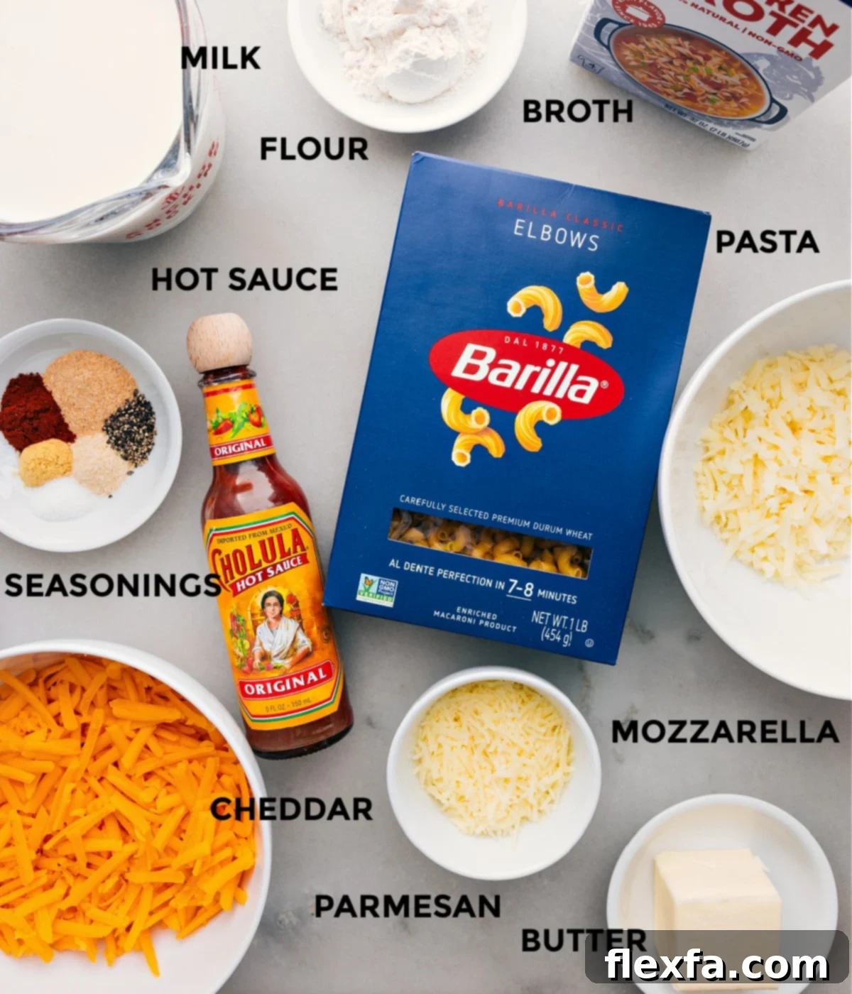 A colorful array of fresh mac and cheese ingredients, including butter, flour, spices, milk, broth, macaroni, and various cheeses, neatly arranged on a counter.