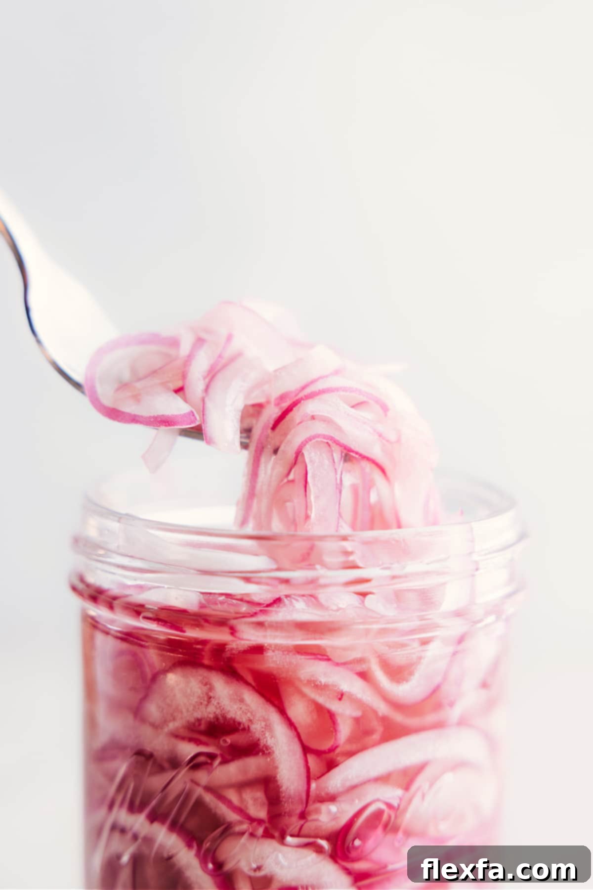 A fork lifting a delicious, juicy cluster of pickled red onions out of a glass jar, highlighting their irresistible texture.