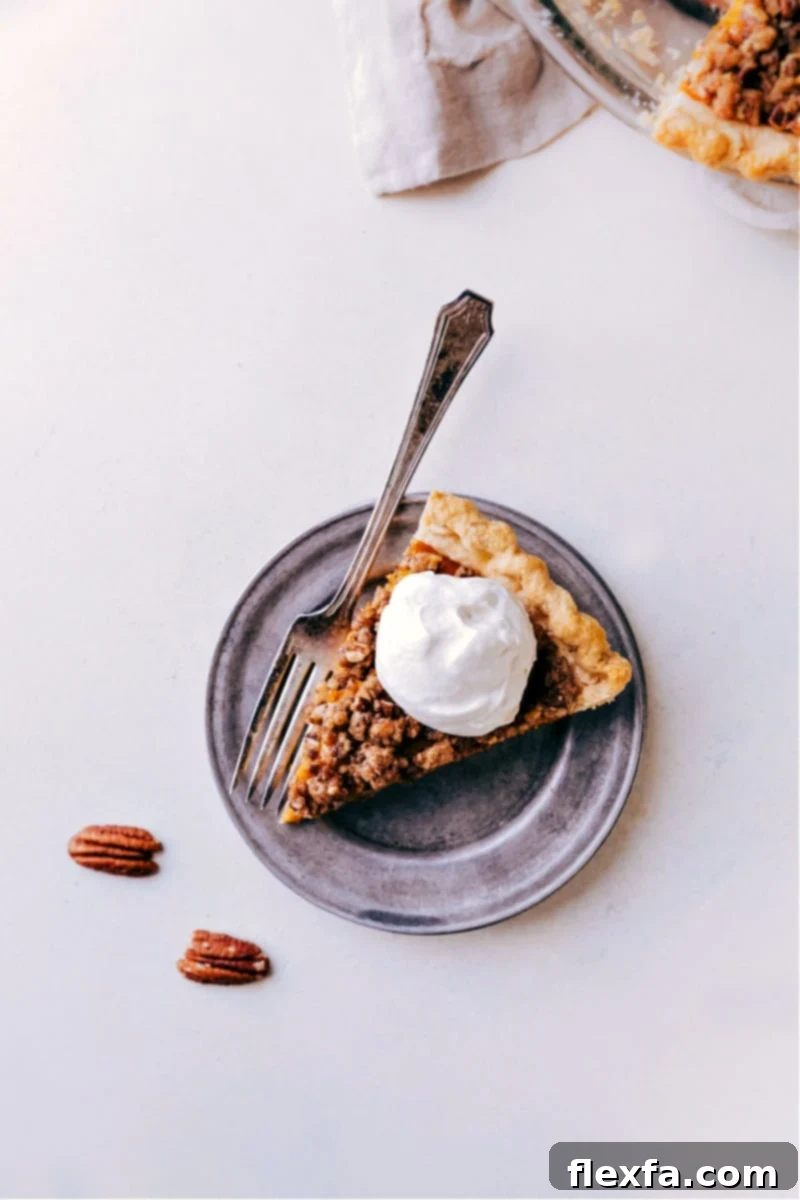 A glorious slice of Pumpkin Pecan Pie, perfectly showcasing its creamy pumpkin filling, golden brown pecan streusel, and a generous dollop of maple whipped cream on top, ready to be enjoyed.