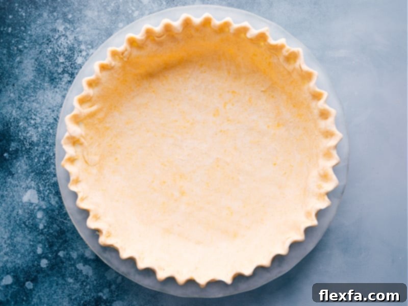 A pristine, unbaked pie crust expertly fitted into a glass pie pan, its edges beautifully crimped and ready to receive the filling. This image highlights the perfect texture and preparation of the homemade crust.