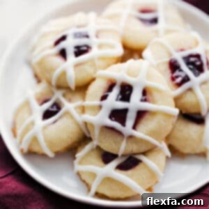Close-up of a raspberry thumbprint cookie, showing the vibrant red jam filling and the delicate almond glaze drizzle.