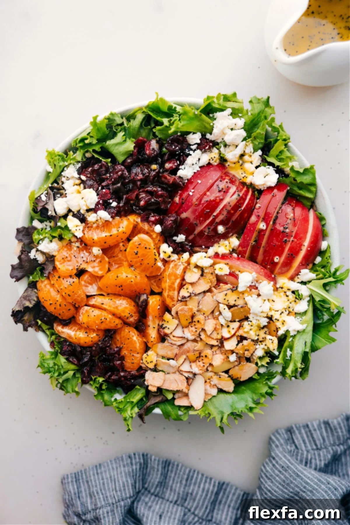 The Best Mandarin Orange Salad Recipe A beautifully arranged Mandarin Orange Salad in a large bowl, dressed and ready to be enjoyed. It features bright orange segments, sliced red apples, green leafy greens, white feta, and glistening candied almonds.