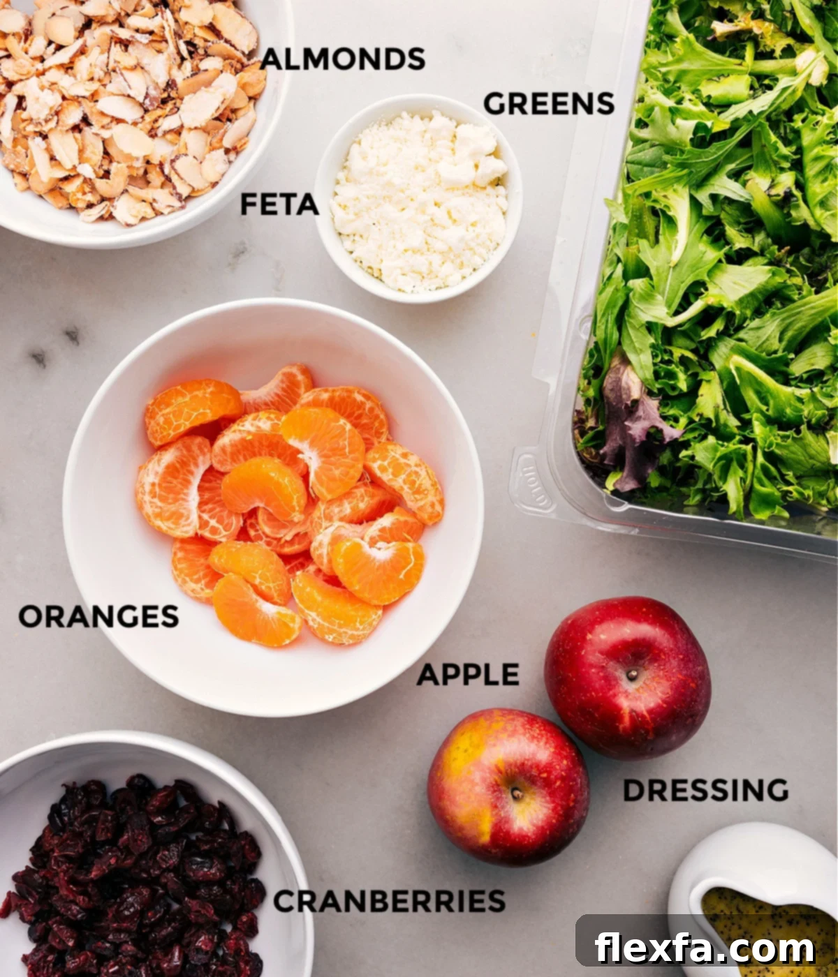 Ingredients In Mandarin Orange Salad Recipe All the fresh and vibrant ingredients for Mandarin Orange Salad prepped and laid out: almonds, mixed greens, segmented oranges, sliced apples, crumbled feta, and dried cranberries, ready for assembly.