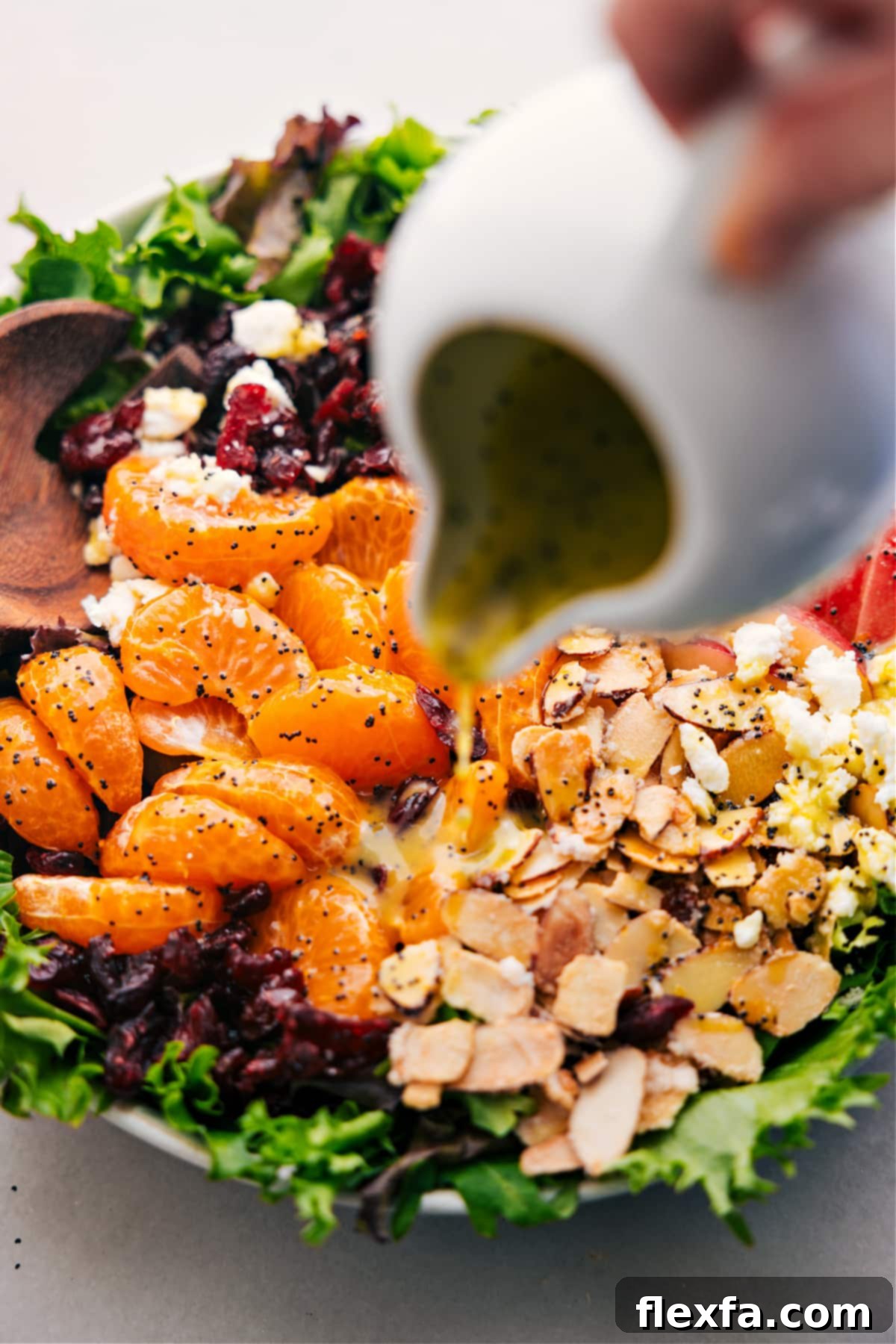 The Easiest And Best Mandarin Orange Salad Recipe Pouring the vibrant citrus poppy seed dressing over the fresh Mandarin Orange Salad in a large serving bowl, ready for a gentle toss.