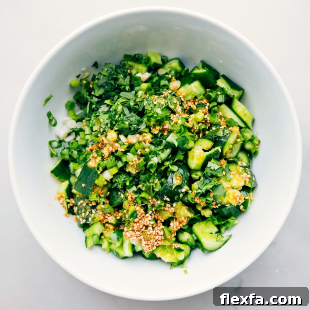 Smashed Cucumber Salad in a bowl, with dressing being poured over and fresh herbs ready to be tossed together for a perfect mix.