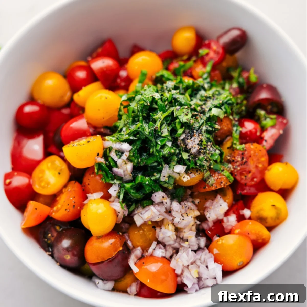 A large mixing bowl filled with all the chopped tomato salad ingredients, including vibrant colorful tomatoes, fresh green basil, and minced aromatics, glistening and ready to be gently tossed with the dressing.