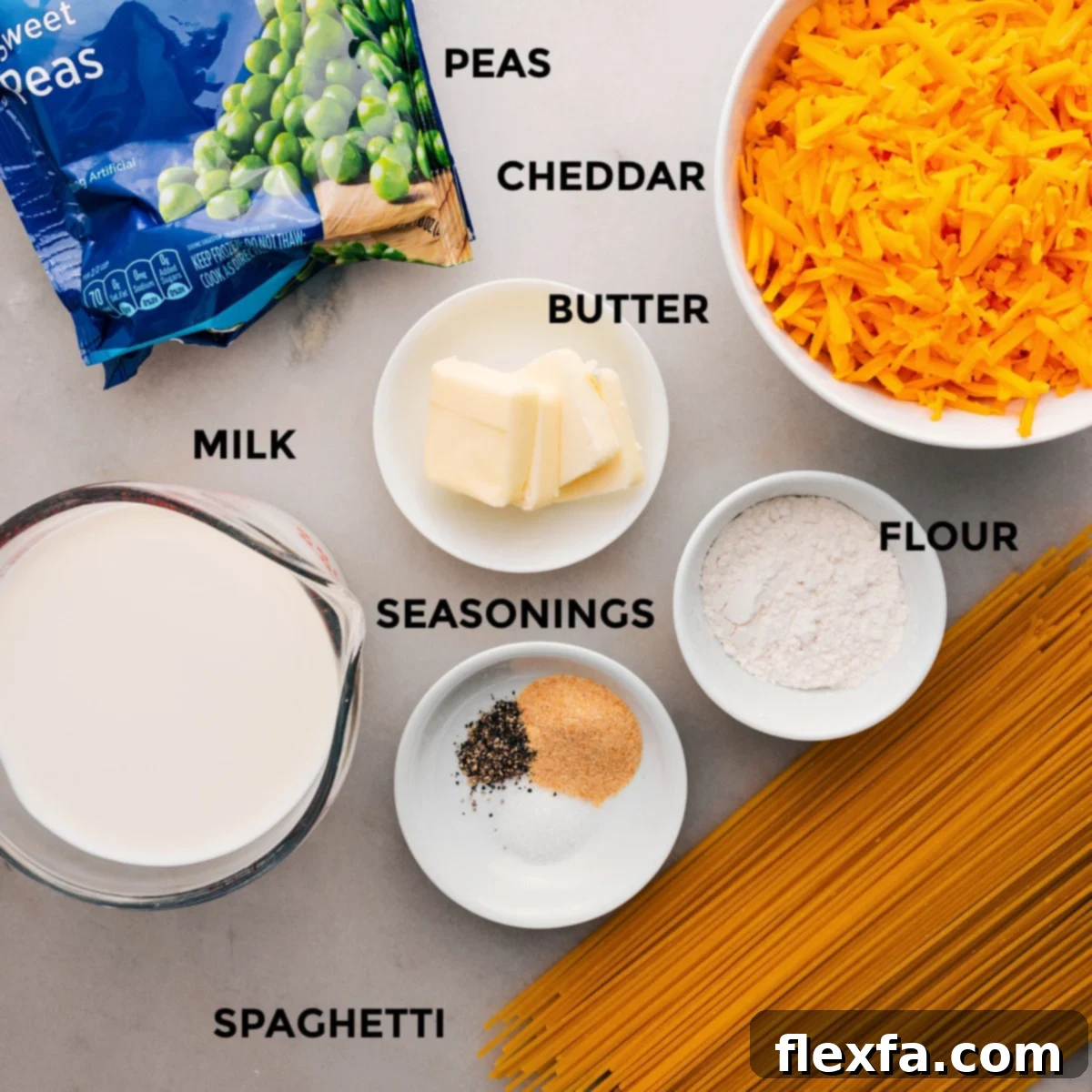 All the essential ingredients for creamy cheesy spaghetti laid out: uncooked spaghetti, fresh block of cheddar cheese, unsalted butter, all-purpose flour, a carton of whole milk, frozen green peas, and common seasonings like garlic and onion powder.