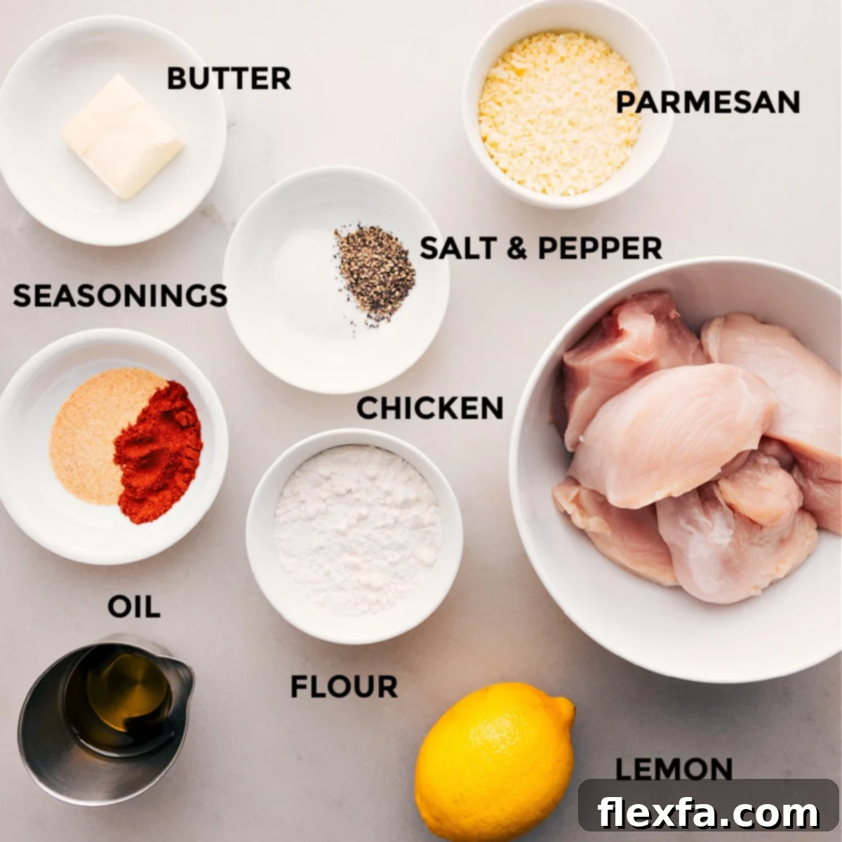 All the ingredients for this recipe are prepped and ready for easy assembly: parmesan, seasonings, chicken, flour, oil, and a lemon.