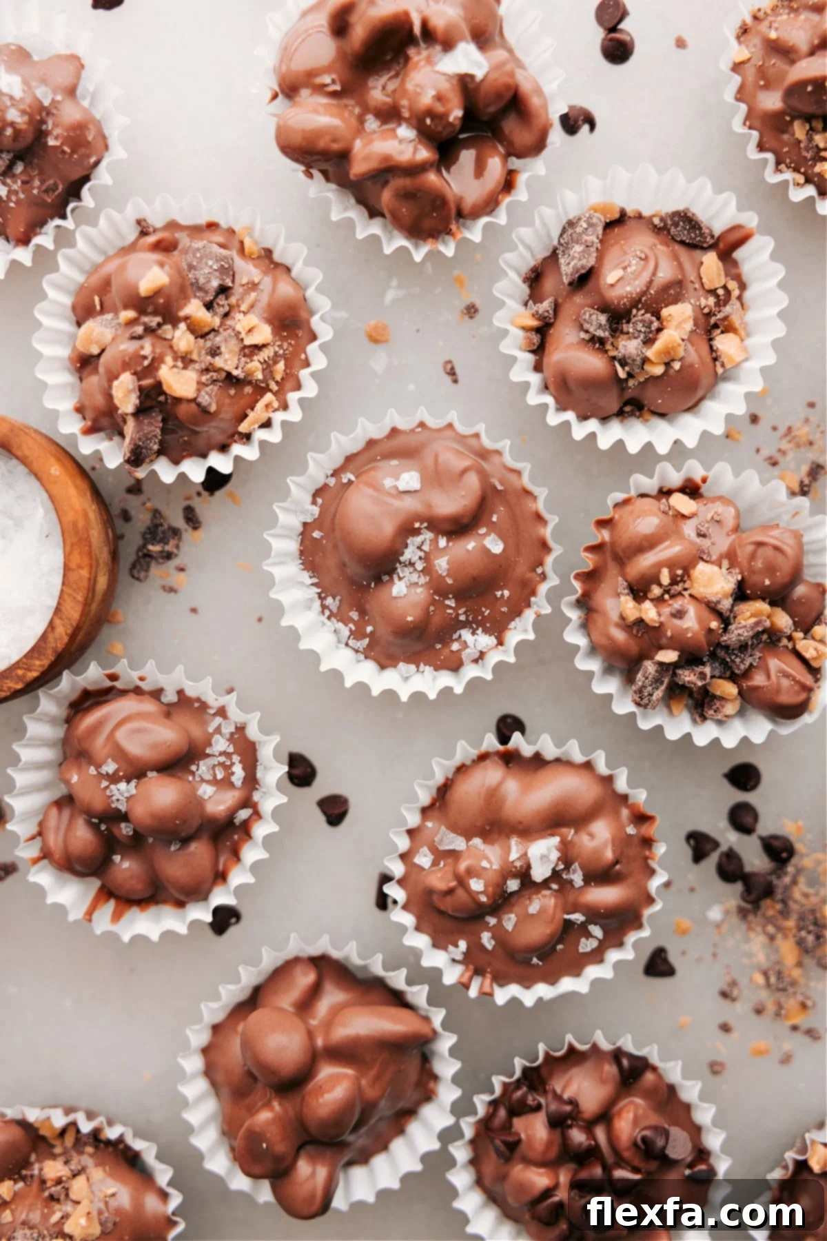 Close-up of Crockpot Candy clusters in mini muffin cups, adorned with crunchy toffee bits and sparkling flaky sea salt, showcasing beautiful presentation.
