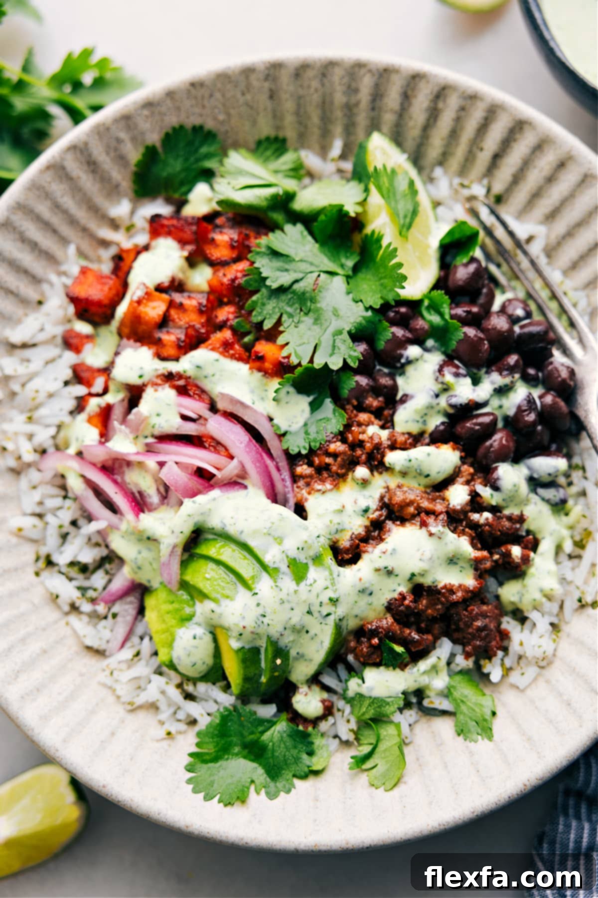 A close-up shot of a beautifully assembled Beef Burrito Bowl, garnished with fresh cilantro, avocado, and a generous drizzle of creamy cilantro-lime sauce, ready to be enjoyed.