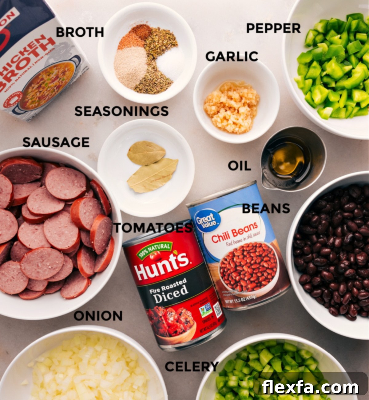 All the fresh ingredients for this black beans and sausage recipe are neatly prepped and laid out for easy assembly: smoked sausage, broth, various seasonings, diced peppers, olive oil, canned beans, and diced tomatoes.