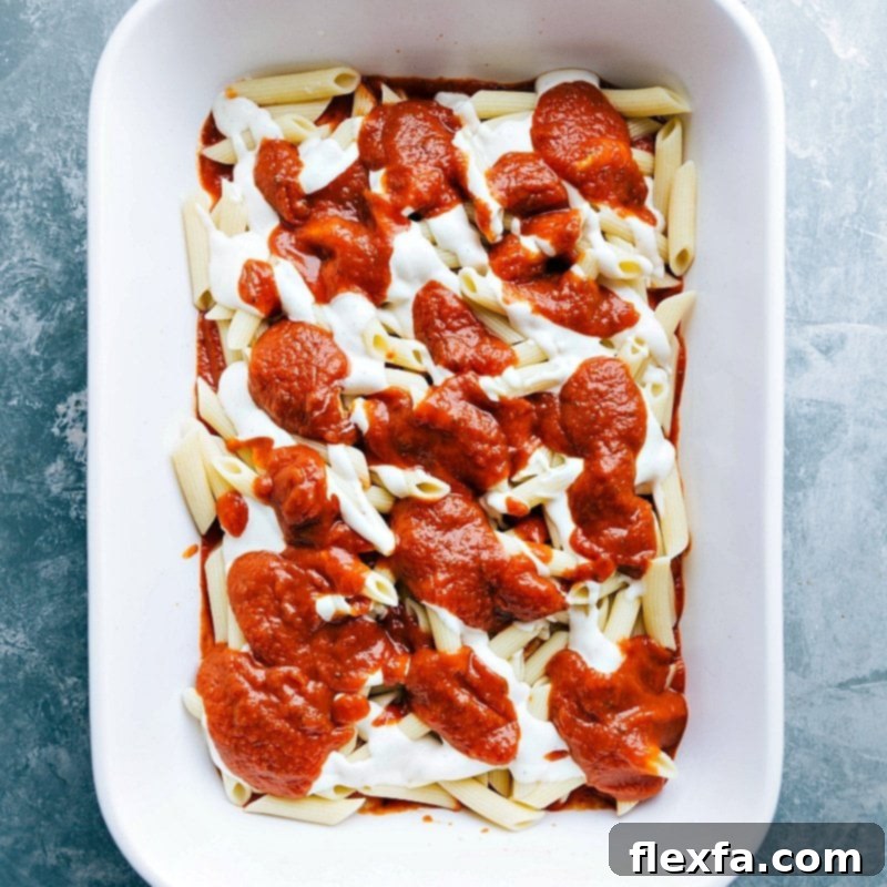Marinara sauce being layered on top of alfredo sauce in a pasta dish, creating a rich flavor combination.
