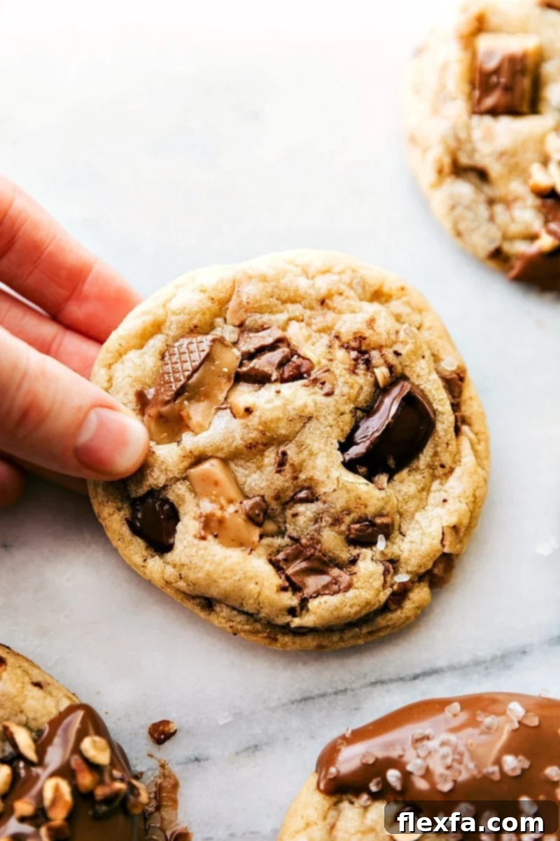 Freshly baked Toffee Cookies held in hand, still warm and ready to be savored. Golden brown with visible chocolate and toffee pieces.