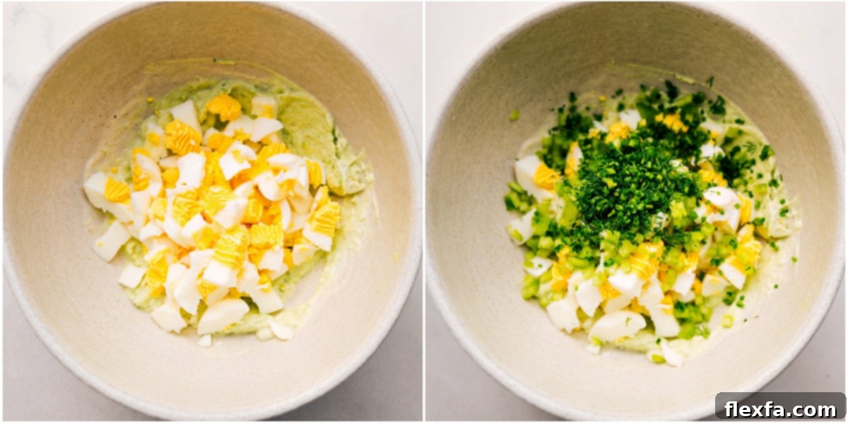 Diced hard-boiled eggs and fresh chopped herbs being added to the mashed avocado base in a bowl, ready to be mixed.