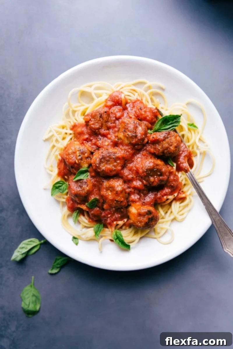 Golden brown Chicken Parmesan Meatballs nestled on a bed of perfectly cooked spaghetti, generously coated in a rich, vibrant red marinara sauce. The dish is beautifully garnished with freshly torn basil leaves and a dusting of grated Parmesan cheese, highlighting its comforting and gourmet appeal.