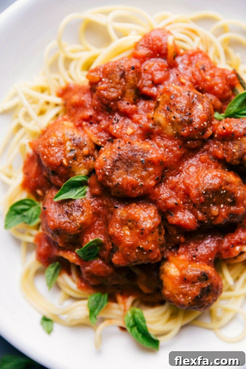 A close-up of a generous serving of Chicken Parmesan Meatballs with pasta, smothered in marinara sauce and topped with fresh basil, ready to be enjoyed as a hearty and comforting Italian meal.