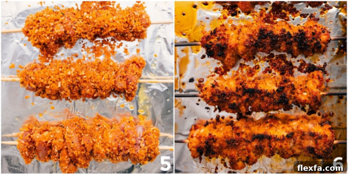Close-up of golden-brown, crispy hot honey chicken pieces threaded onto metal skewers and arranged on a foil-lined baking sheet after cooking.