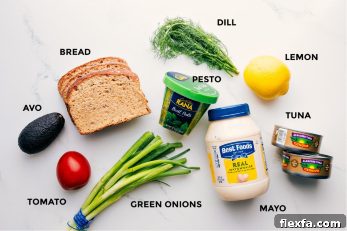 Ingredients In Tunacado All the fresh ingredients meticulously prepped for easy assembly of the homemade Tunacado sandwich, including perfectly sliced avocado, juicy tomato, thin bread, vibrant green onions, fragrant pesto, fresh dill, a lemon for zesty flavor, high-quality tuna, and creamy mayonnaise.