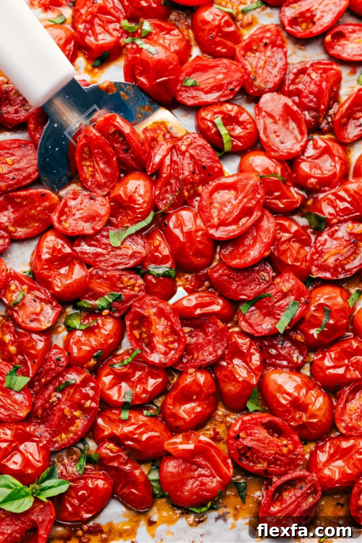 Roasted Cherry Tomatoes on a sheet pan, with a spatula lifting a portion to show their rich color and texture.