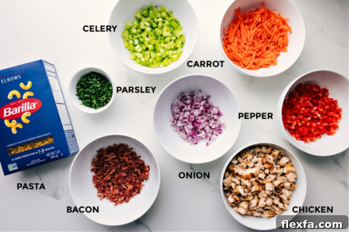 Fresh and Flavorful Ingredients In Chicken Macaroni Salad All the fresh ingredients for Chicken Macaroni Salad are neatly prepped and arranged on a counter, including cooked elbow macaroni, diced chicken, crumbled bacon, grated carrots, diced red bell pepper, chopped celery, red onion, and fresh parsley.
