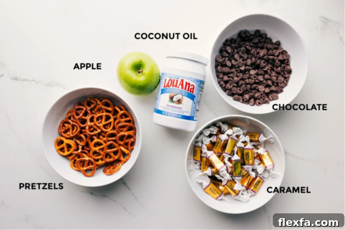 A vibrant flat lay showing all the key ingredients for Caramel Apple Bark prepped and ready: chocolate chips, coconut oil, mini pretzels, a sliced Granny Smith apple, soft caramels, heavy cream, and flaky sea salt.