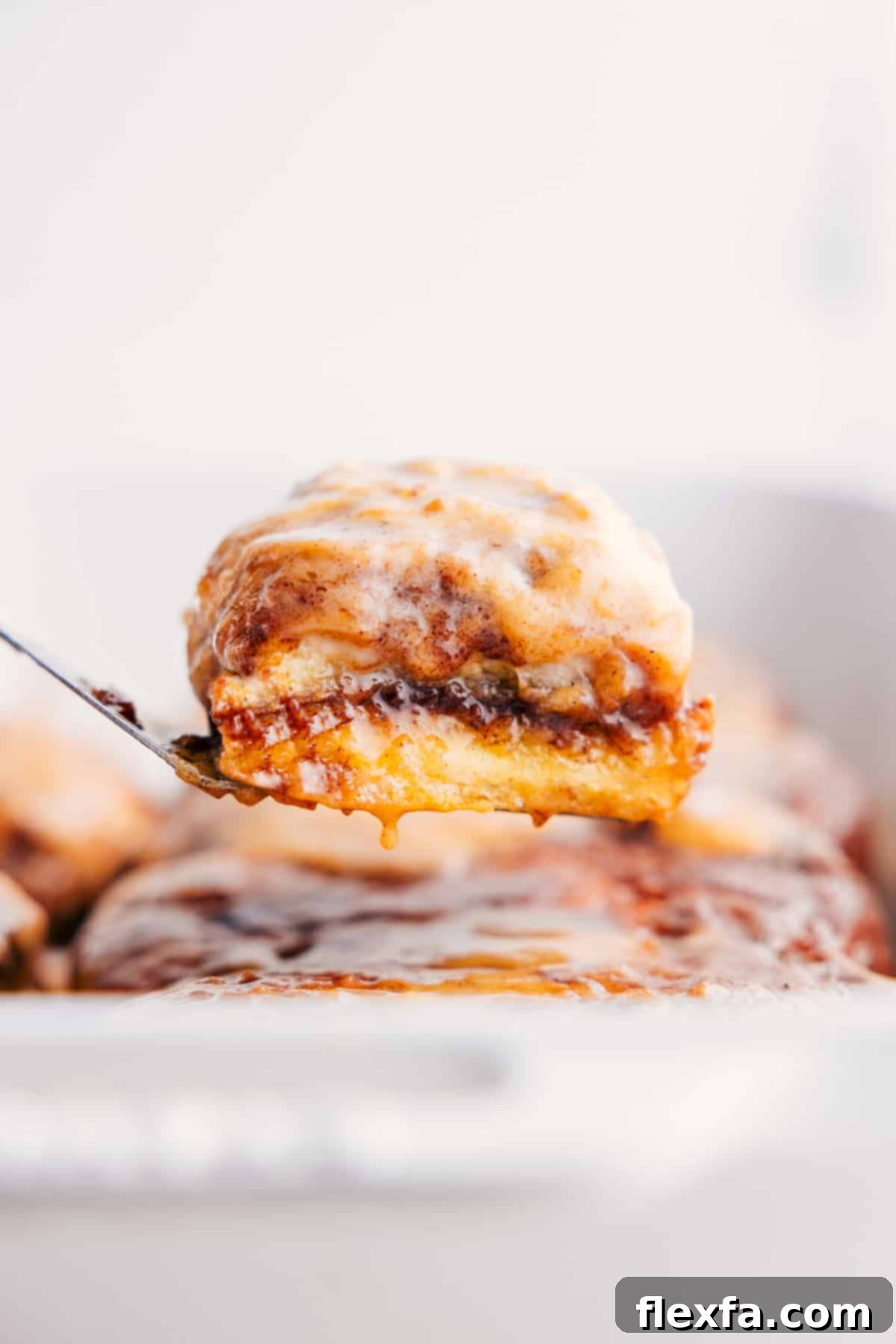 Irresistibly soft and gooey magic pumpkin cinnamon rolls being pulled from a baking pan, generously drizzled with a decadent cream cheese glaze.