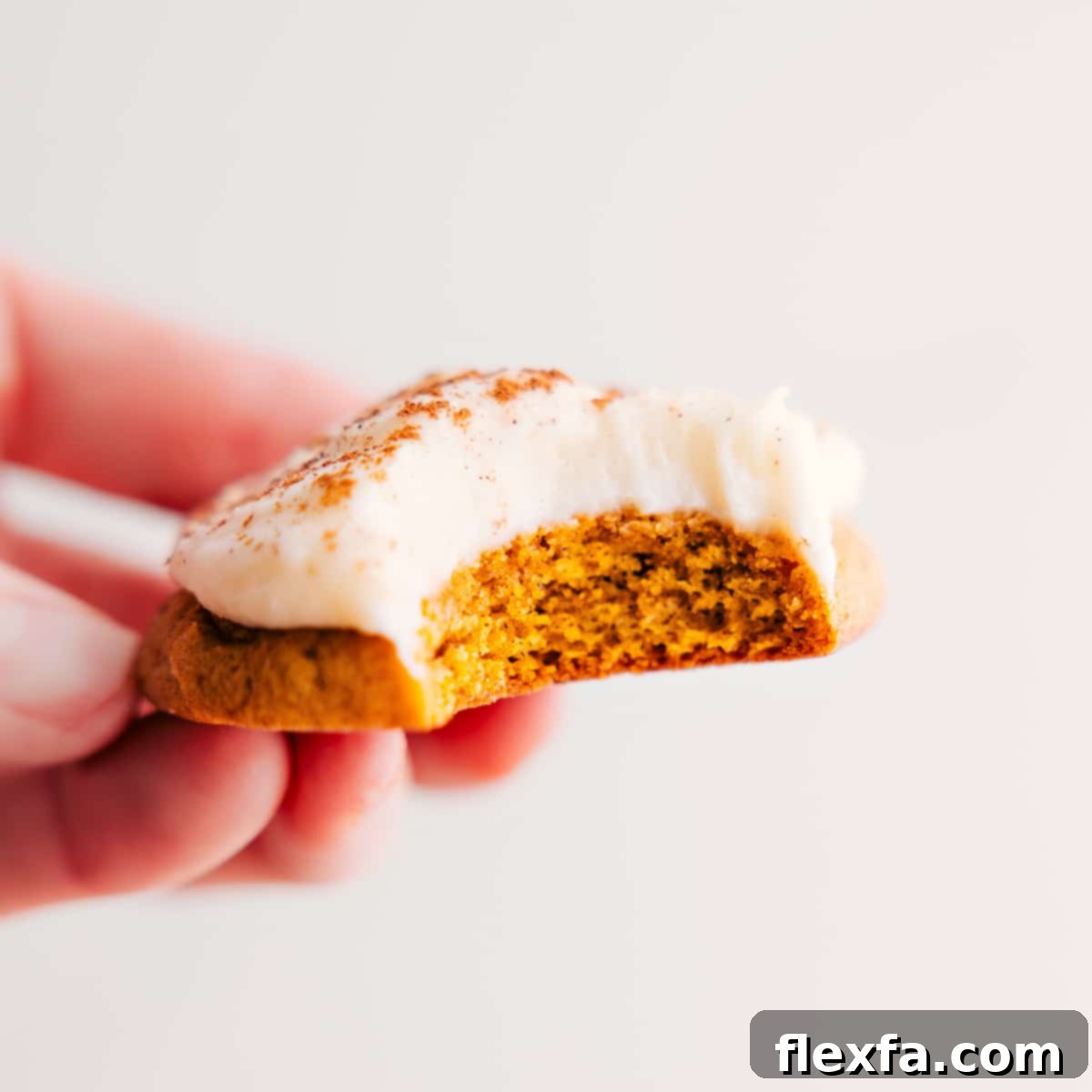 A soft, round pumpkin cookie generously topped with creamy cream cheese frosting, with a delightful bite taken out.
