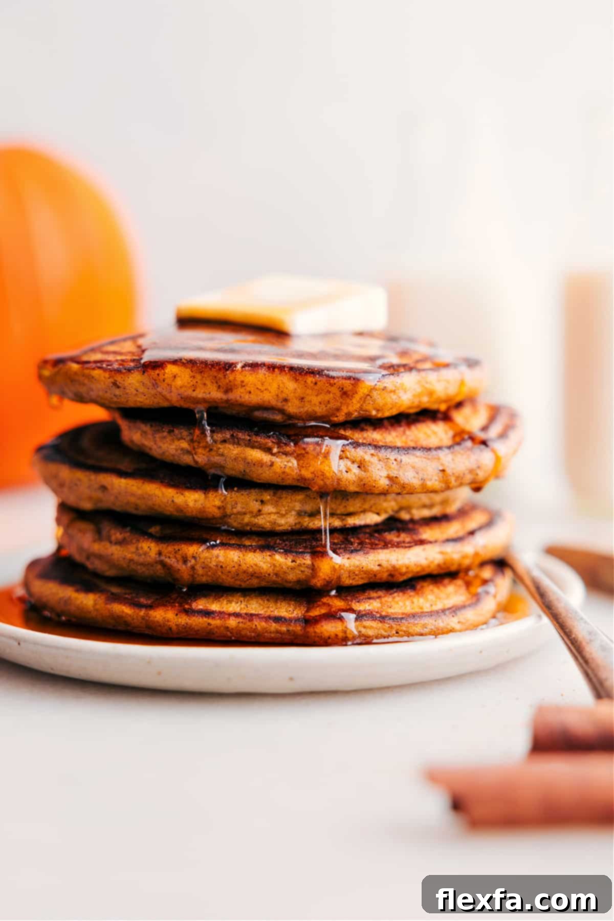 A mouthwatering stack of fluffy pumpkin pancakes, generously topped with a pat of melting butter and drizzled with golden maple syrup.