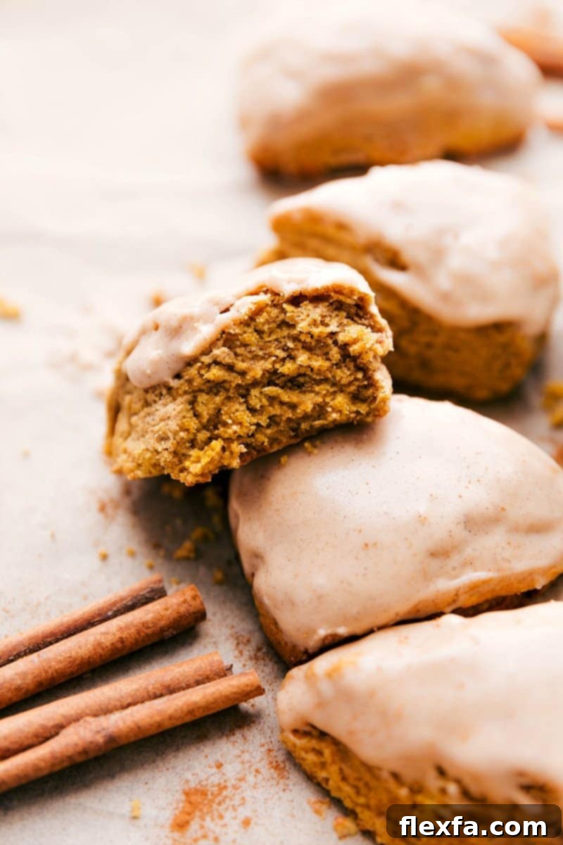 Delightful pumpkin scones featuring a generous, glistening glaze on top, with one scone showcasing a perfect bite.