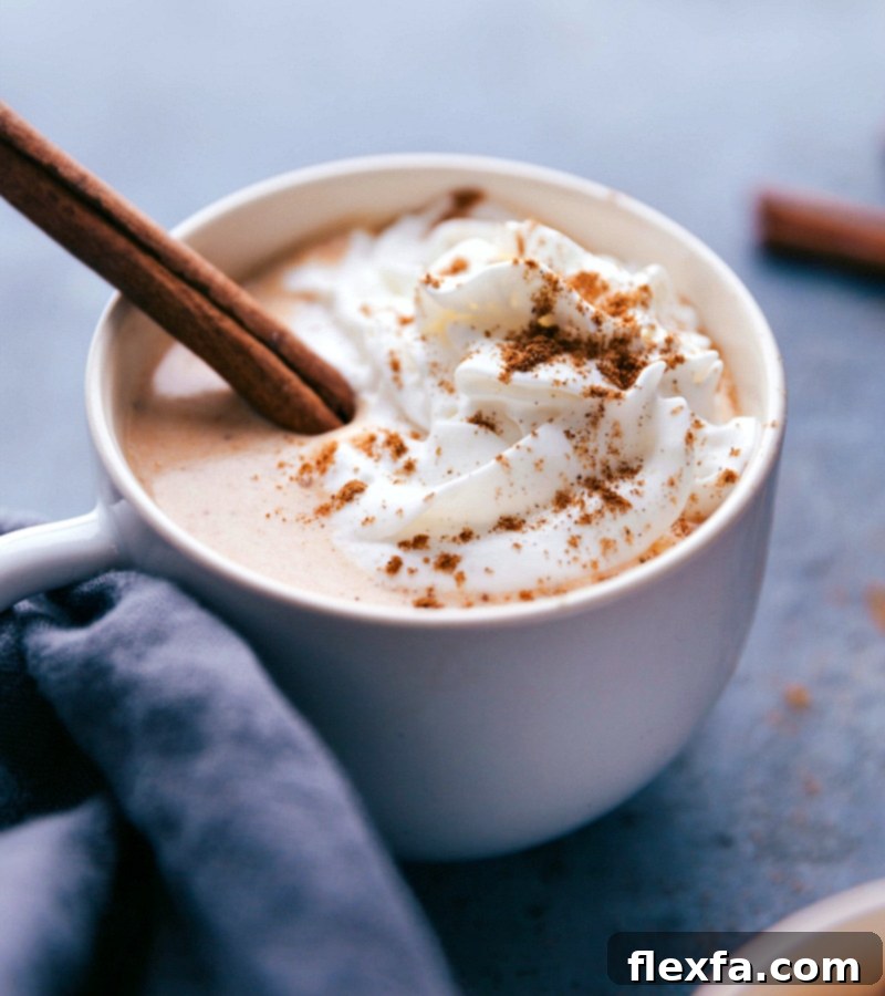 A cozy pumpkin spice latte steamer, elegantly topped with whipped cream, a sprinkle of pumpkin pie spice, and a cinnamon stick garnish.