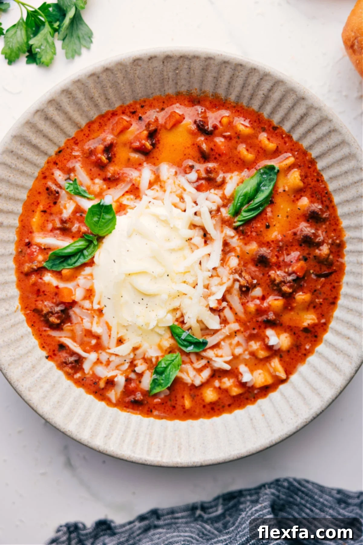 A beautifully presented bowl of Crockpot Lasagna Soup, garnished generously with freshly grated cheese and vibrant basil leaves, steaming and ready to be savored as a comforting and delicious meal.