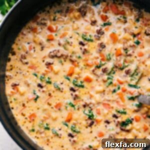 A close-up of a serving of Creamy Parmesan Italian Sausage Soup in a bowl with a spoon.