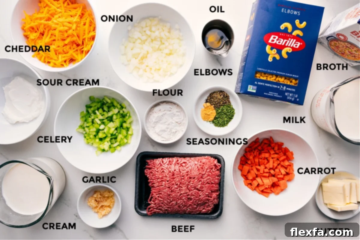 All the ingredients for this recipe prepped and ready for easy assembly, including sour cream, cream, cheddar, onion, celery, garlic, flour, ground beef, seasonings, oil, carrot, milk, butter, pasta, and broth.