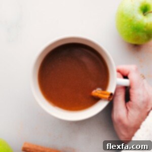Hand holding a warm cup of apple cider with steam rising, a perfect comforting image.