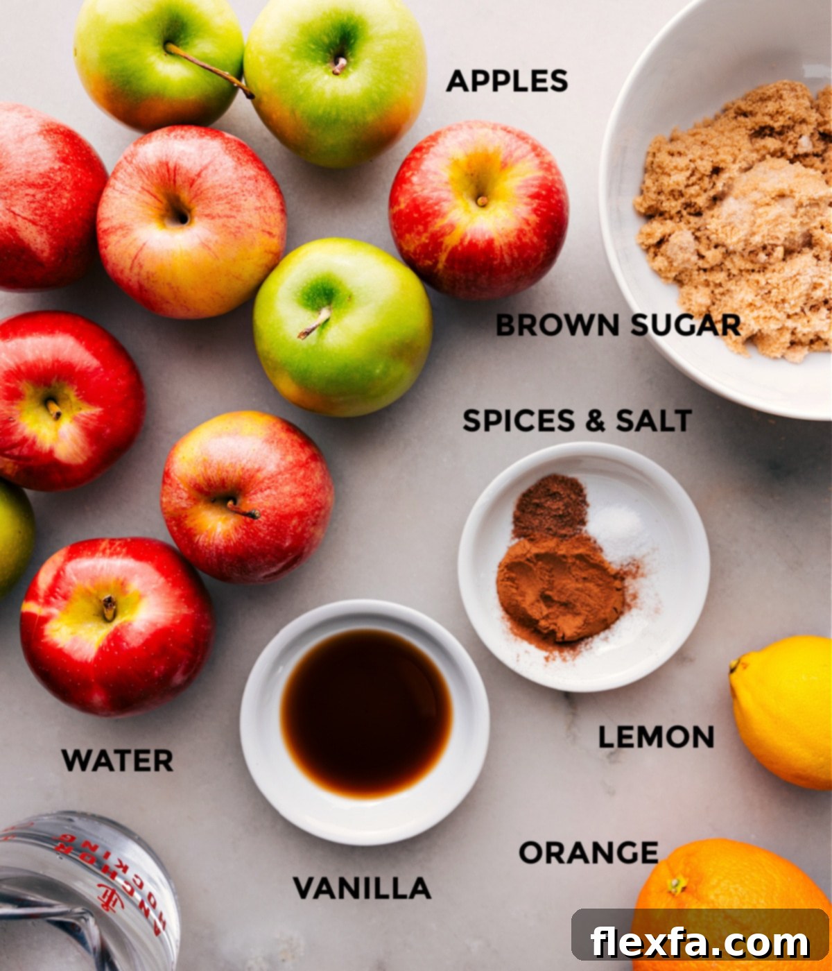 A vibrant display of fresh ingredients: apples, an orange, brown sugar, vanilla extract, and whole spices, ready for making homemade hot apple cider.