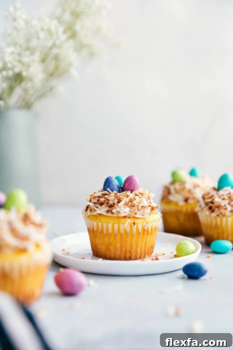 Four beautifully decorated bird's nest Easter cupcakes with yellow cake, cream cheese frosting, toasted coconut, and M&M's candy eggs.