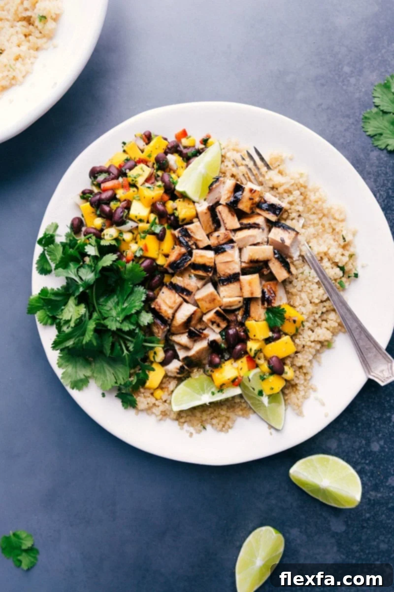 Delicious chicken quinoa bowl with fresh mango salsa, cilantro, and lime wedges, showcasing a vibrant and healthy meal.