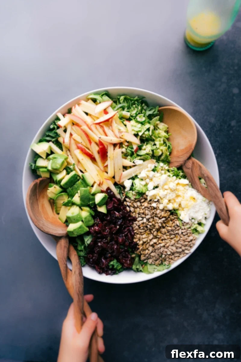 A beautifully presented Brussels sprout salad in a large bowl, garnished with colorful and healthy ingredients like shredded greens, apple slices, cranberries, and feta.
