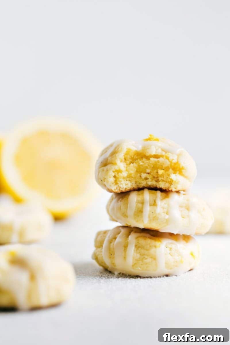 Stacked Lemon Cheesecake Cookies with a Bite Taken Out of One A stack of three lemon cheesecake cookies topped with a delicious frosting with a bite taken from the top cookie, showcasing its soft interior.