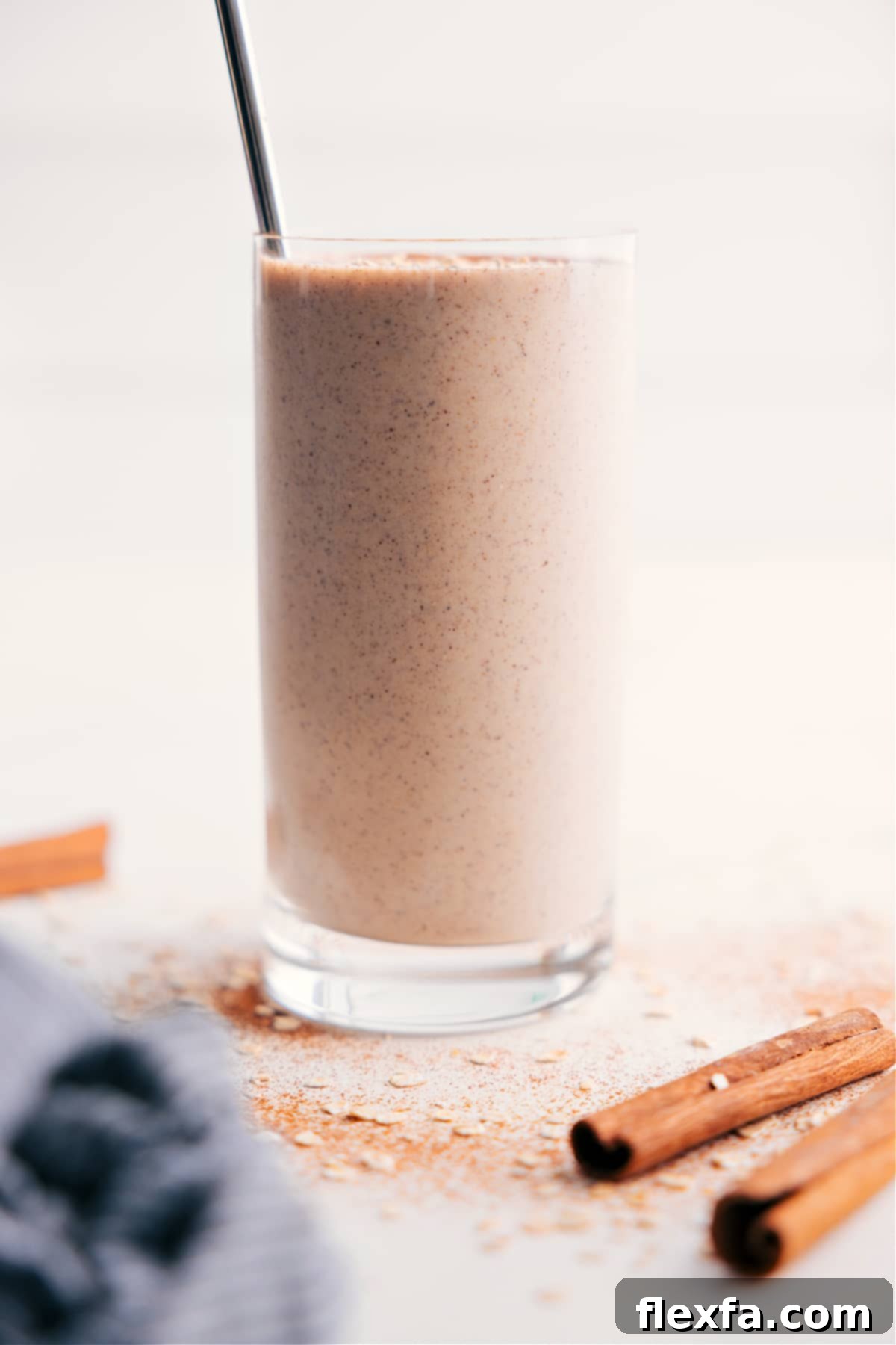 Creamy oatmeal smoothie in a glass with a straw, garnished with a sprinkle of cinnamon.