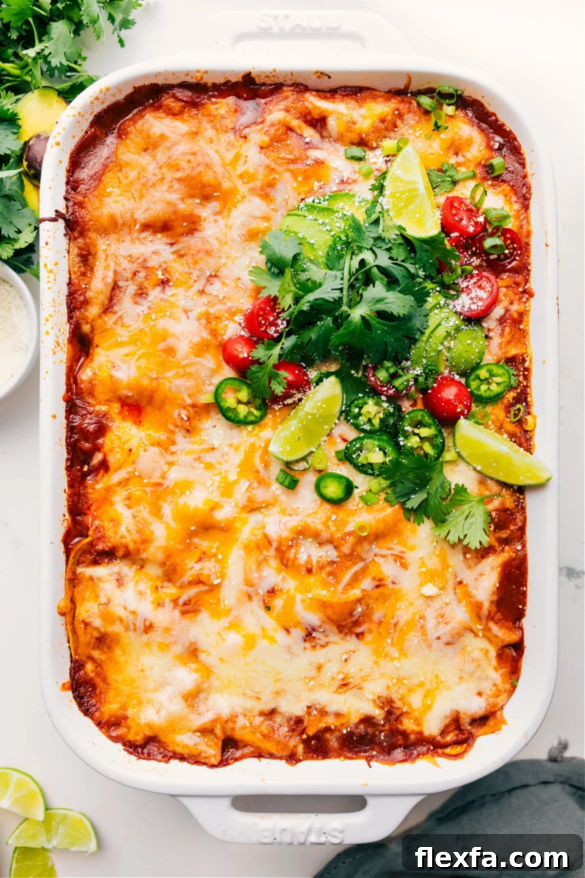 Chicken Enchilada Casserole just out of the oven, topped with fresh cilantro, diced avocado, chopped tomatoes, and lime wedges.