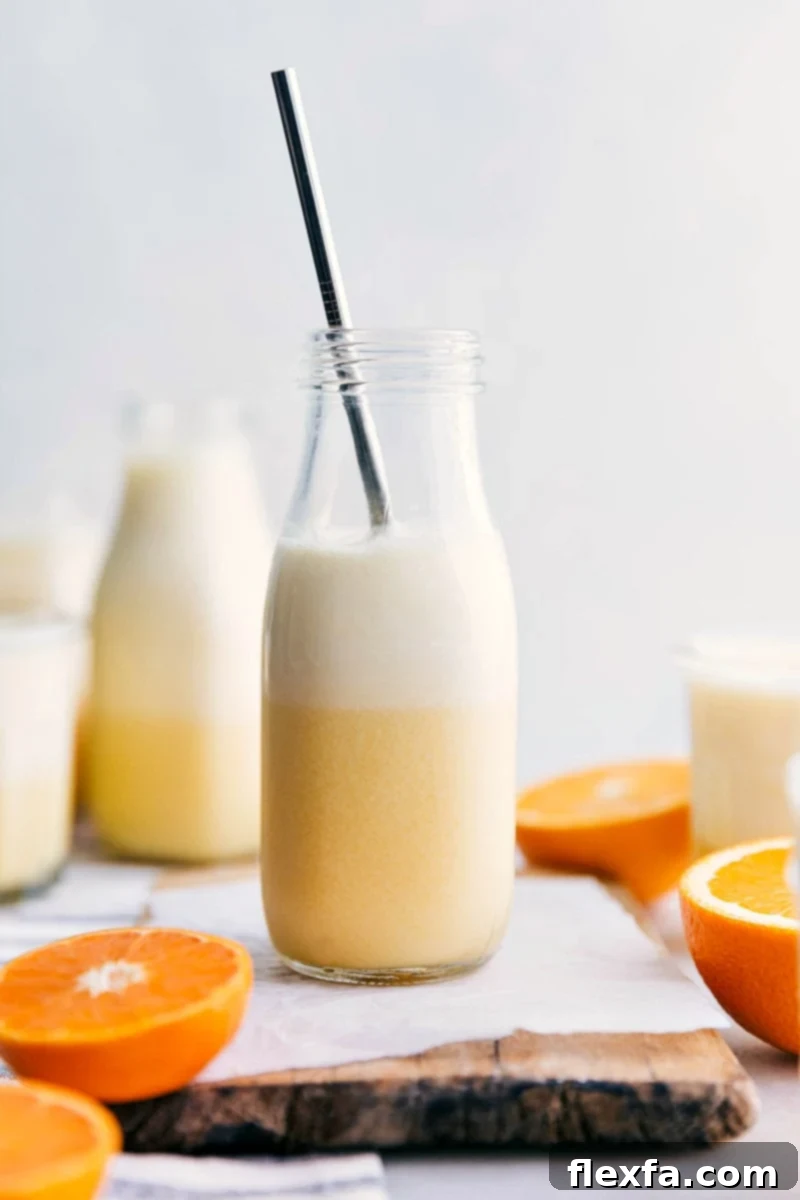 Our Favorite Homemade Orange Julius Recipe, garnished and ready. Ready-to-drink Orange Julius with a straw in it and cut oranges around it, set on a bright surface.