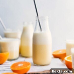 Orange Julius in a glass, with fresh orange slices beside it.