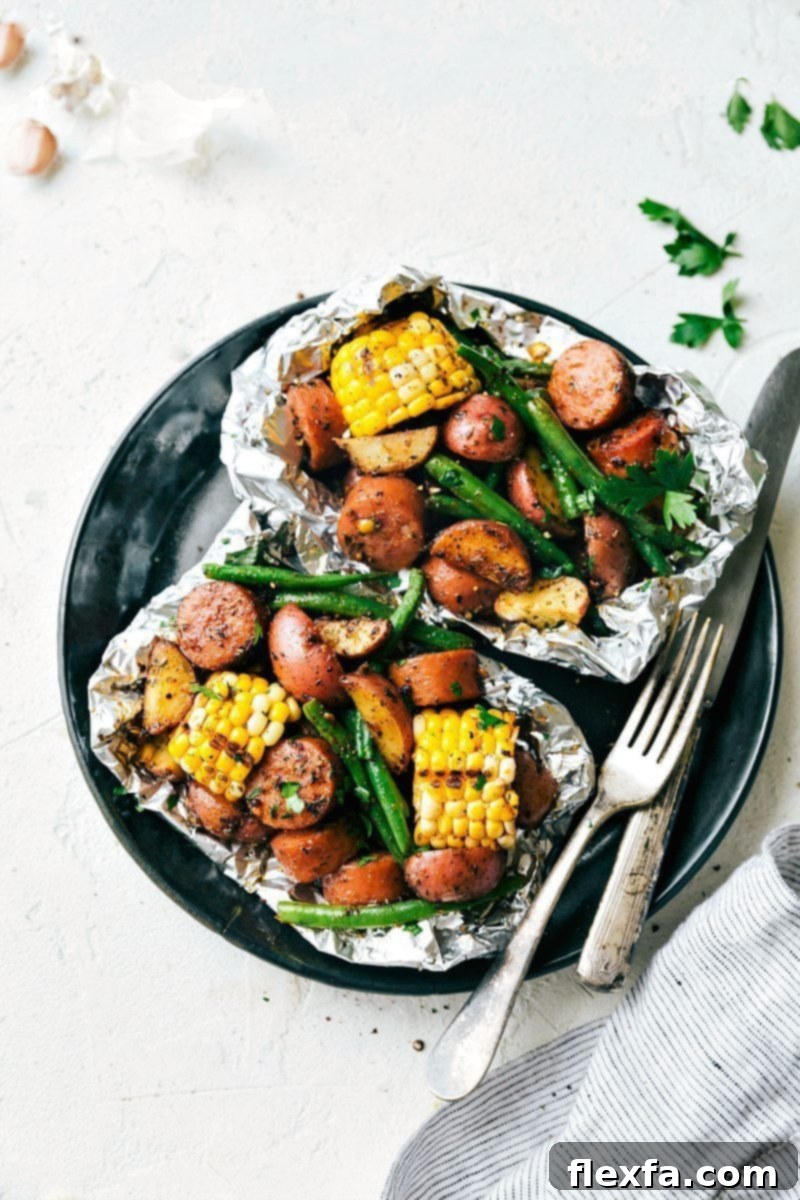 Overhead image of two perfectly cooked garlic butter sausage and veggies in individual foil packs, garnished with fresh herbs, ready to be served from the grill or oven.