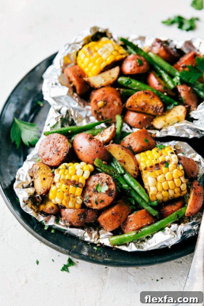 Two deliciously cooked foil packs of garlic butter sausage and veggies, garnished generously with fresh parsley and grated Parmesan cheese, showcasing a flavorful, easy, and satisfying meal ready to be enjoyed straight from the packet.