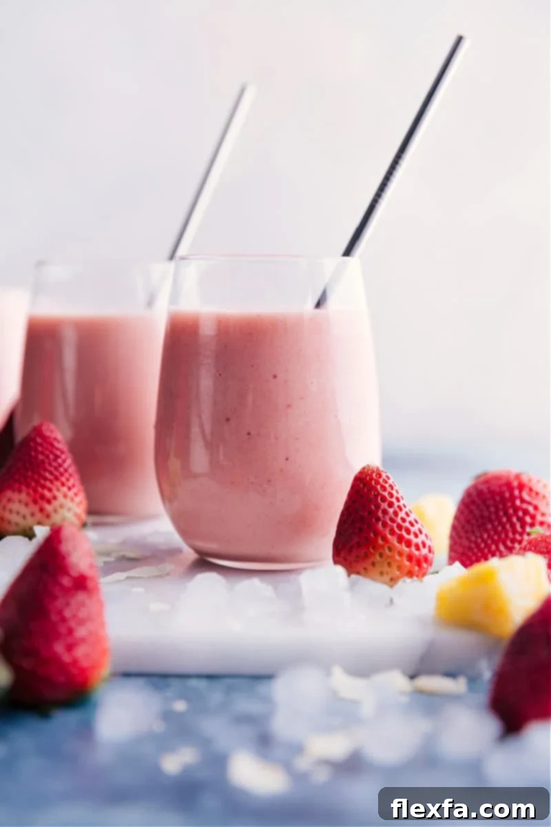 Delicious and refreshing Strawberry Piña Colada smoothies, a perfect non-alcoholic blend of coconut, pineapple, and strawberries. Two tall glasses filled with creamy, pink Strawberry Piña Colada smoothies, garnished with fresh strawberries and pineapple wedges, evoking a tropical and refreshing vibe.