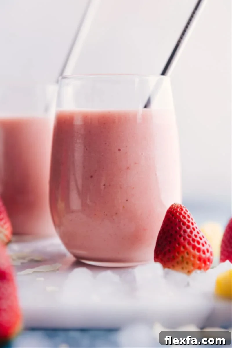 Beautifully presented Strawberry Piña Colada smoothies, ready to be enjoyed. Two vibrant Strawberry Piña Colada smoothies in elegant tall glasses, garnished with fresh fruit and a tropical backdrop, ready to be enjoyed.