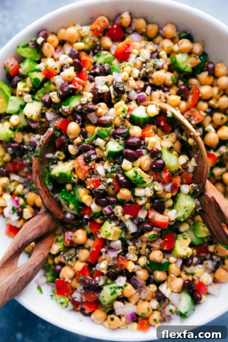 Overhead image of a colorful Garbanzo Bean Salad in a large bowl, garnished with fresh parsley, with serving spoons ready.